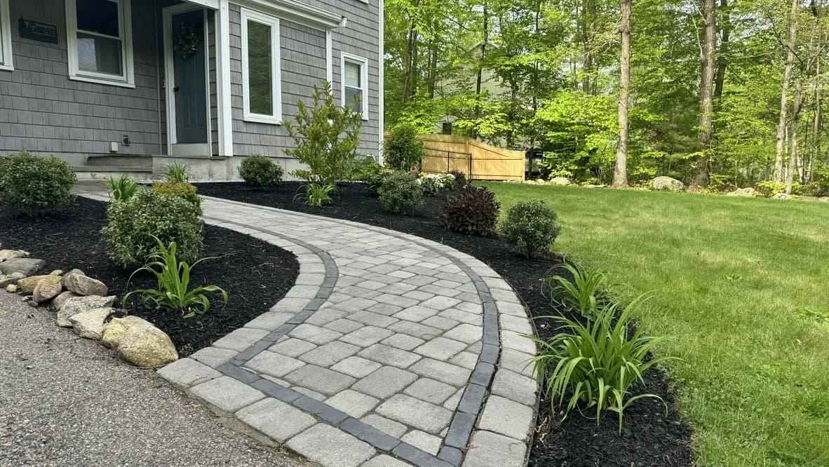 Curved gray paver walkway with a dark accent border, shrubs, and fresh mulch beside a front porch