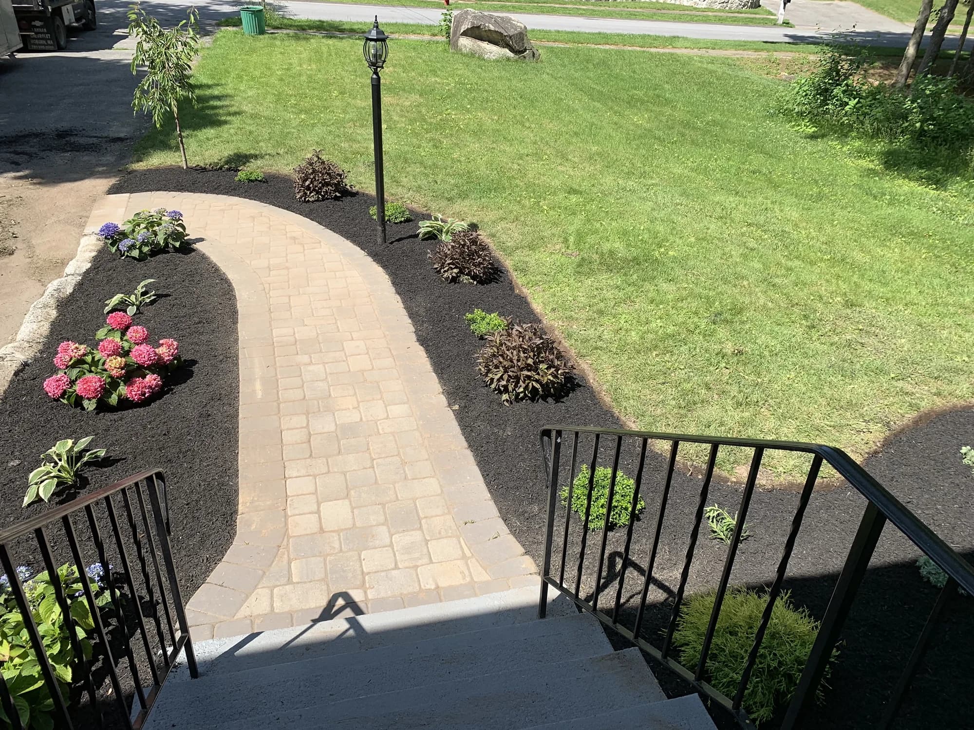 View from front steps over a curved paver walkway bordered by hydrangeas and mulched beds
