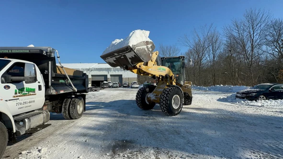 Wheel loader lifting a bucket of snow into a dump truck at a commercial property