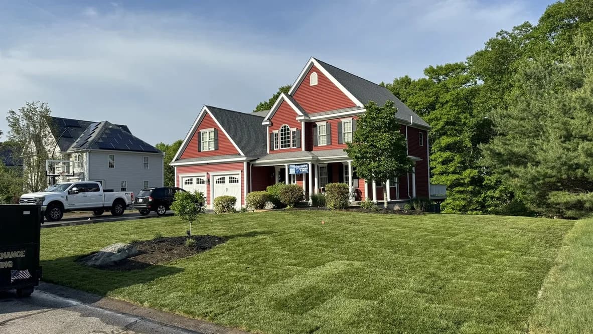 Green front lawn surrounding a young tree and mulched bed at a red colonial-style house
