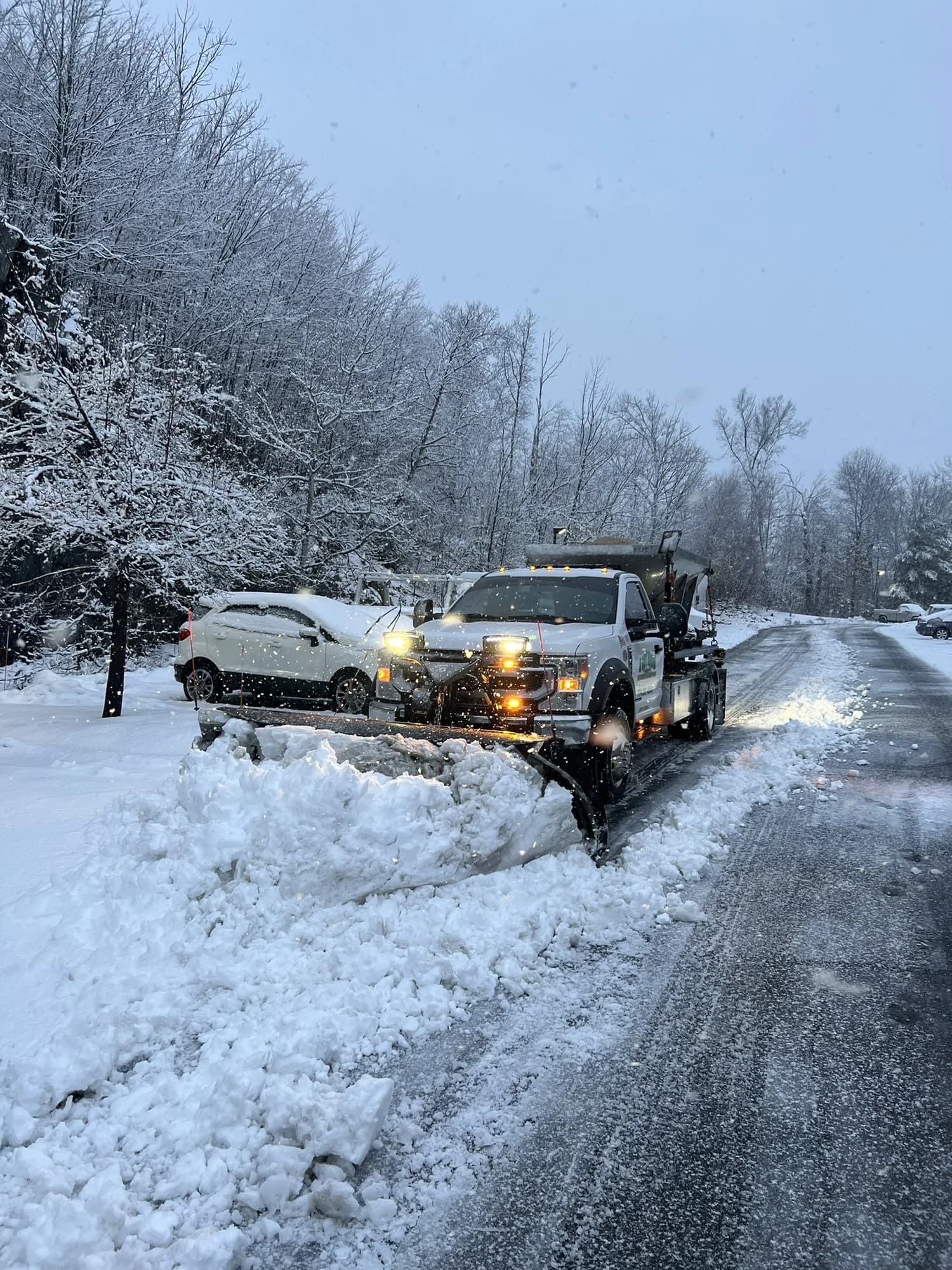A Cut Above plow truck pushing deep snow along a tree-lined access road