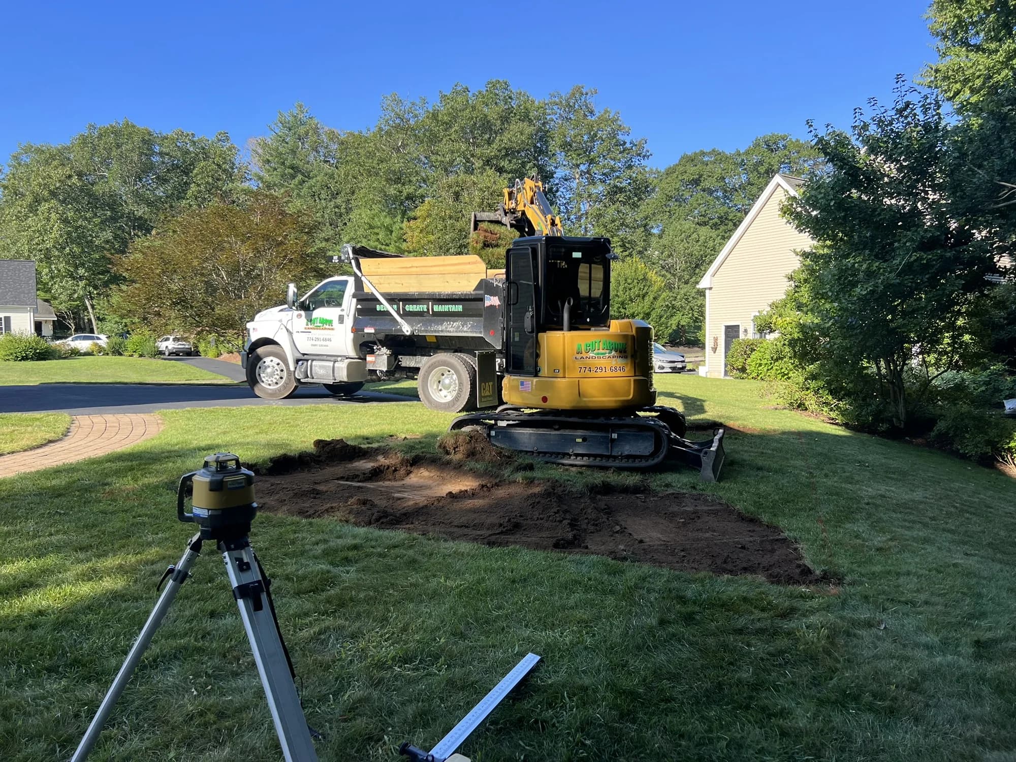 Compact excavator, dump truck, and grade-leveling equipment at a residential excavation project
