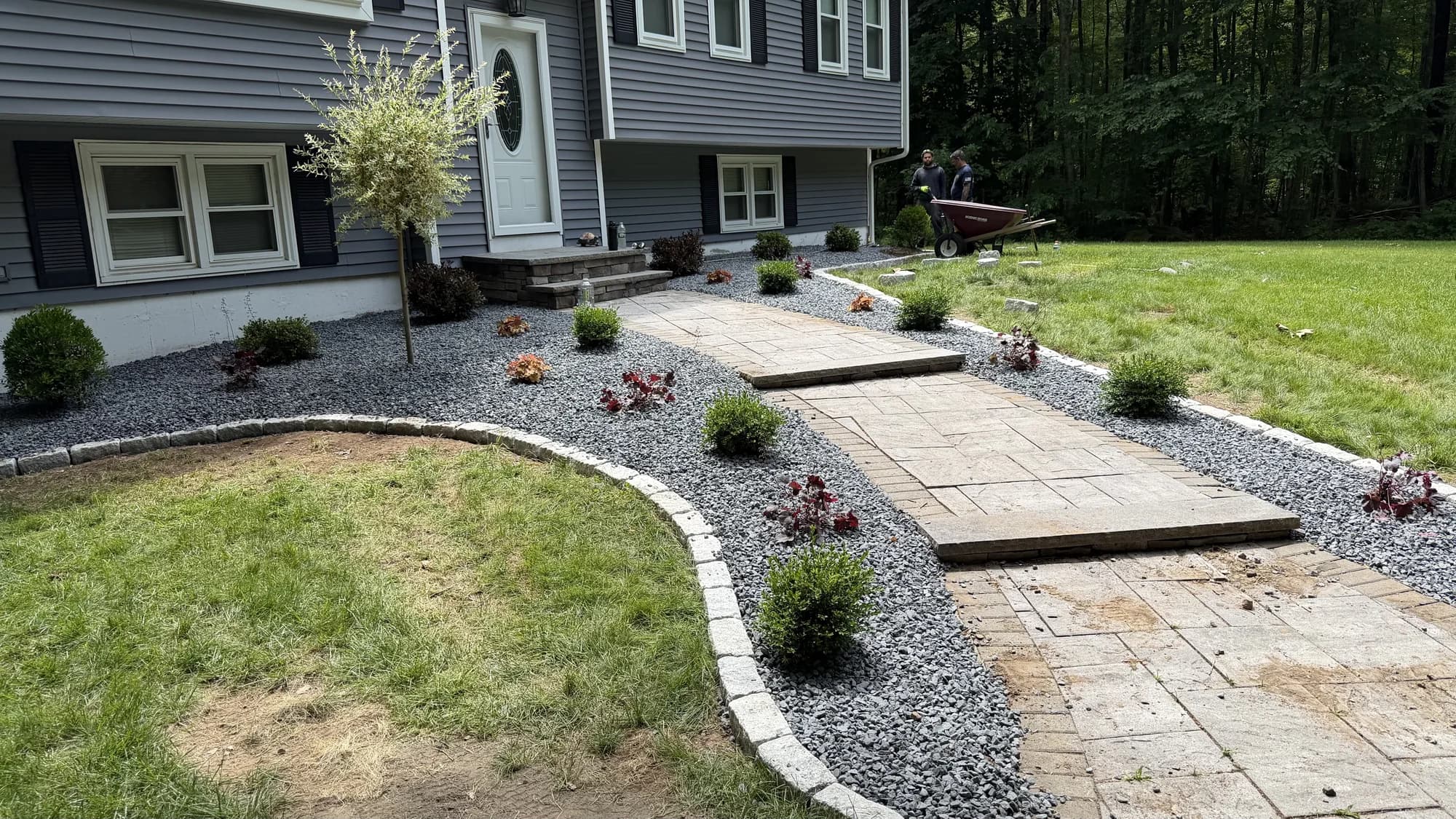 Stepped paver walkway approaching a front door through stone-covered planting beds