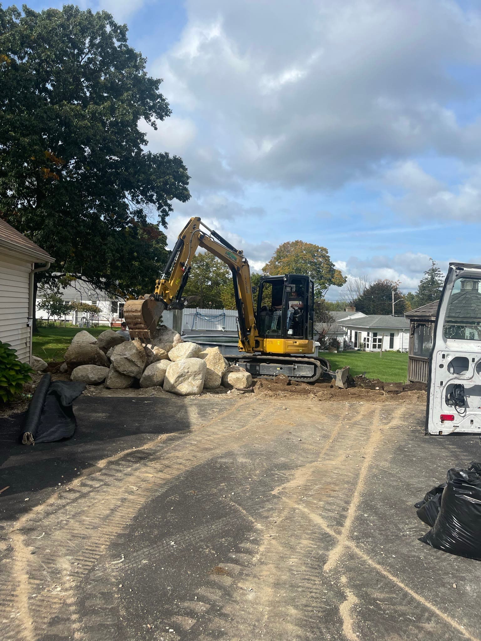 Compact excavator positioning boulders during residential sitework