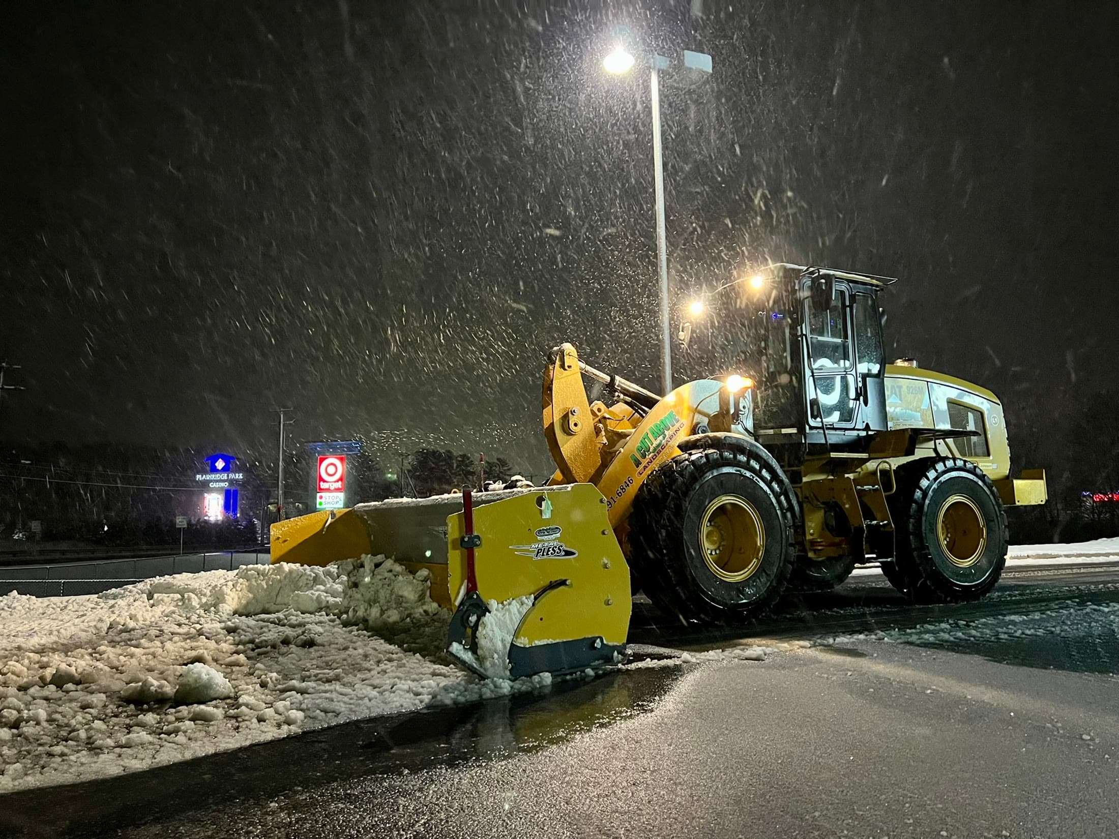 Wheel loader clearing a commercial parking area during active snowfall
