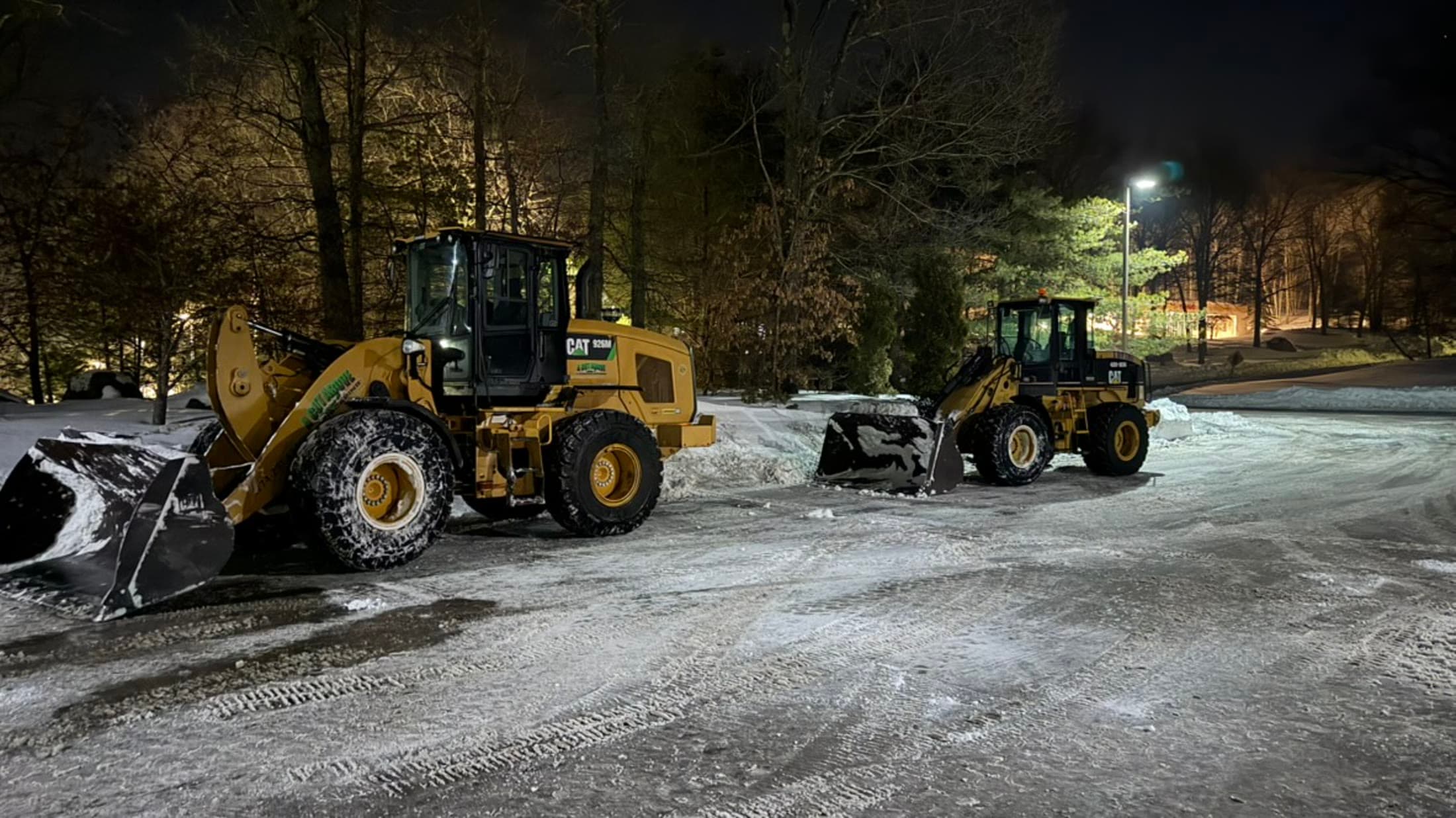 Two wheel loaders clearing snow from a commercial parking area at night