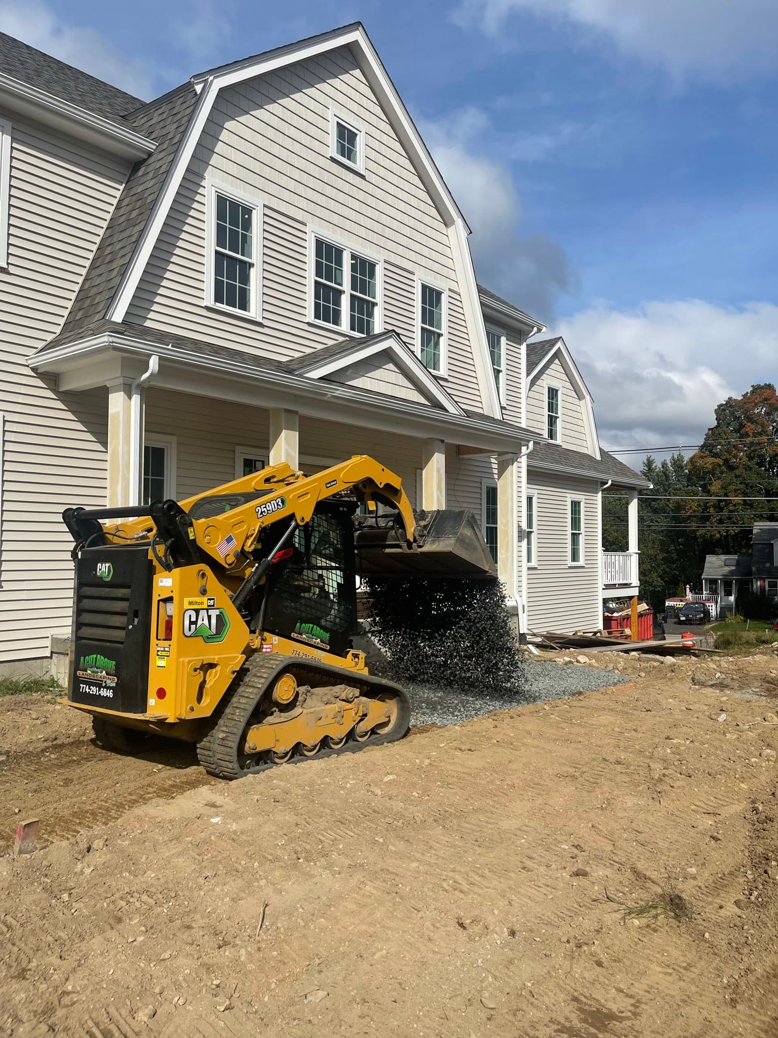 Compact track loader placing crushed stone beside a residential building