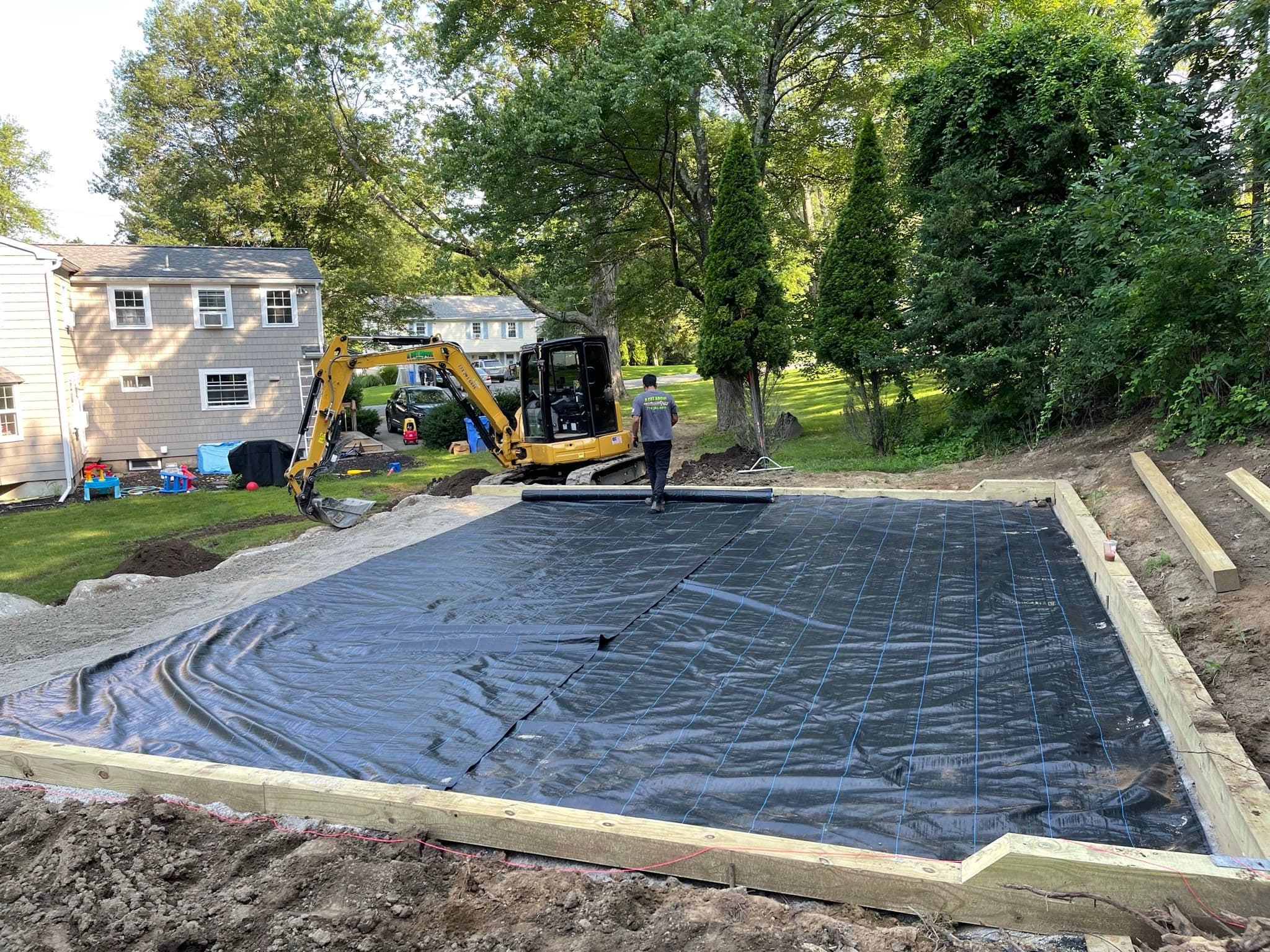 Excavator preparing a framed and compacted stone base on a residential property