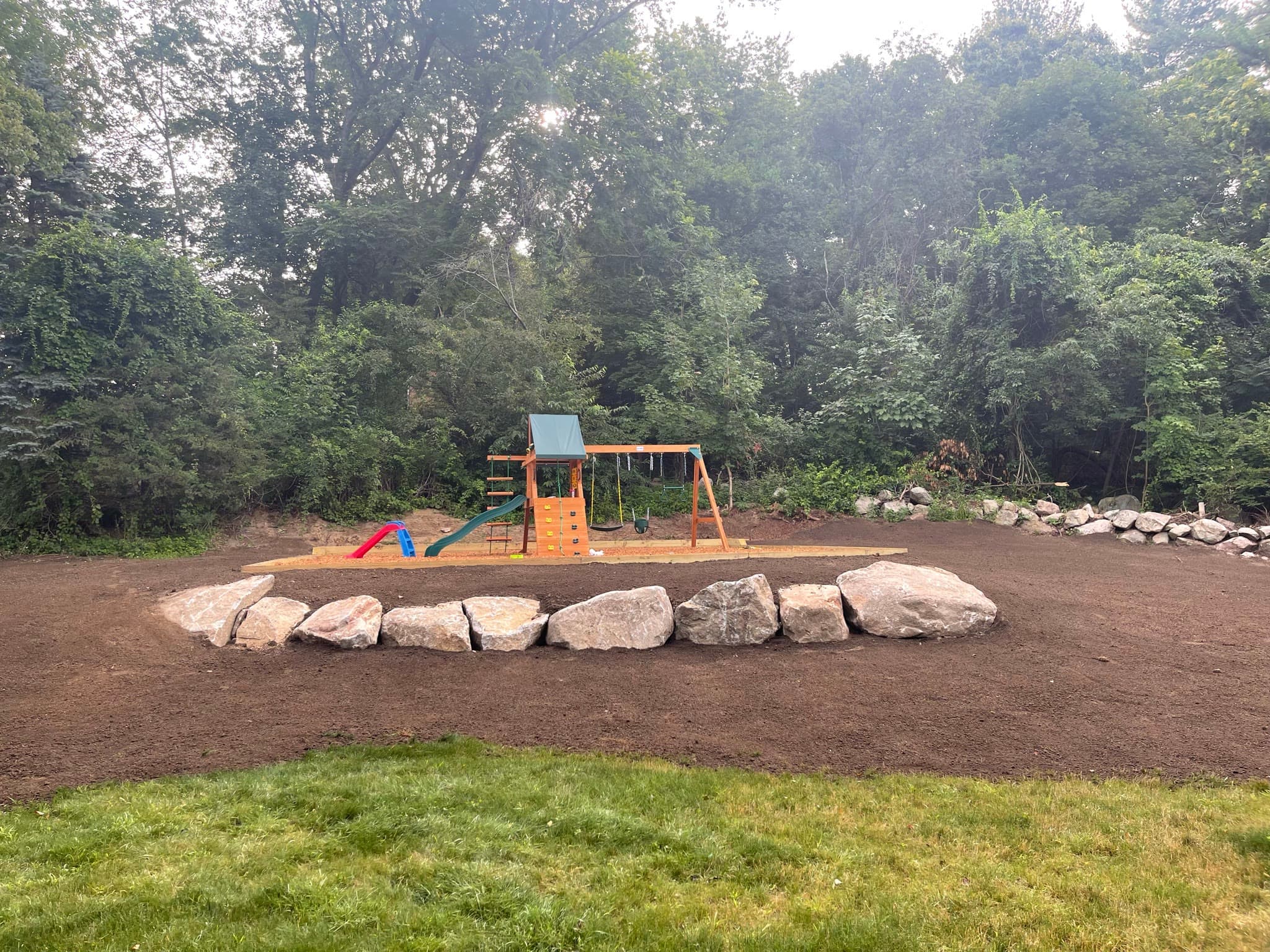 Finished residential yard with a natural boulder border and prepared play area