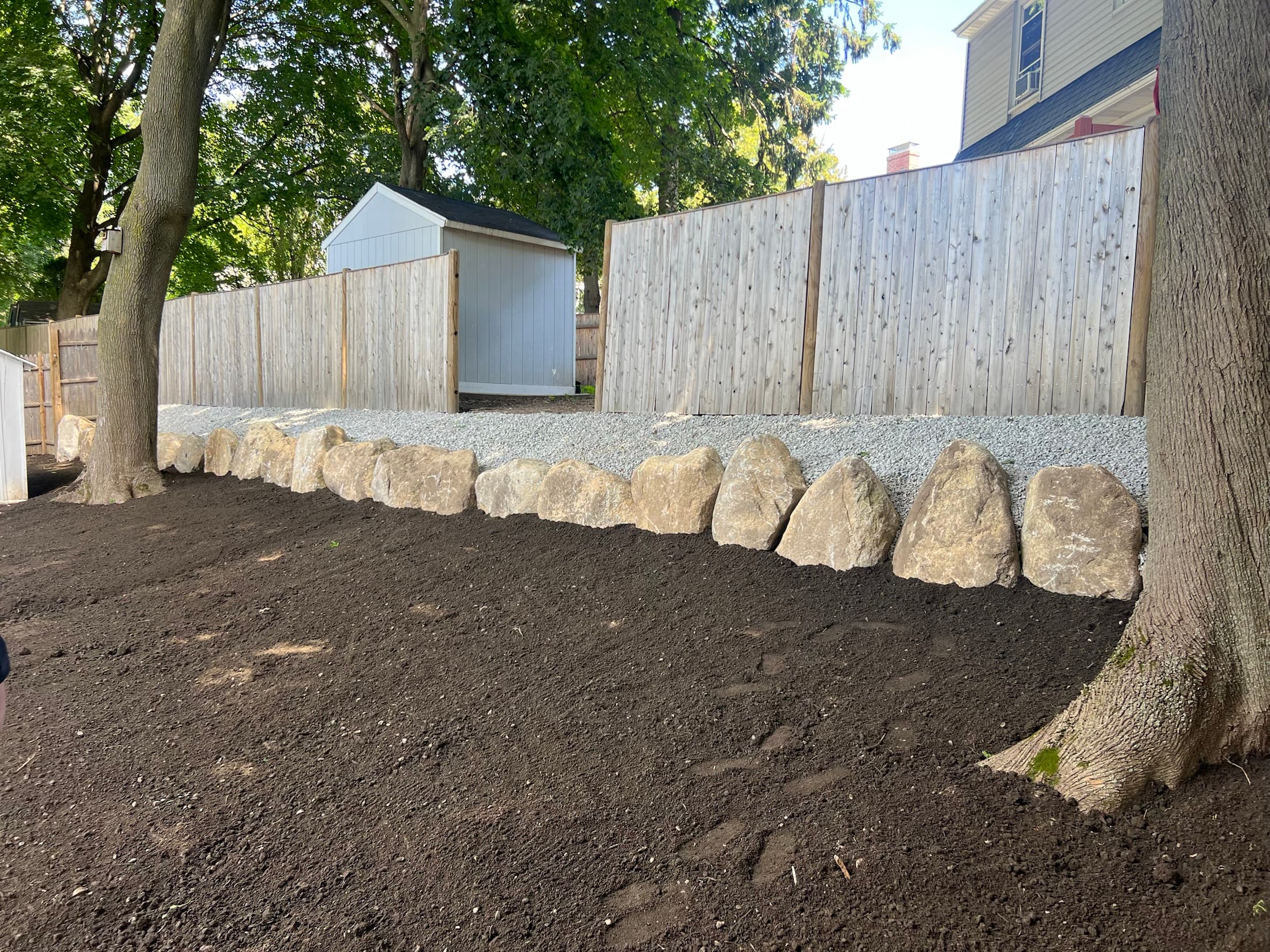 Finished residential grading with a natural boulder border and crushed stone behind a wood fence