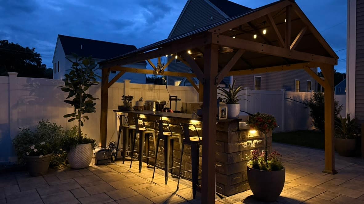 Finished outdoor kitchen and paver patio beneath a lighted pavilion