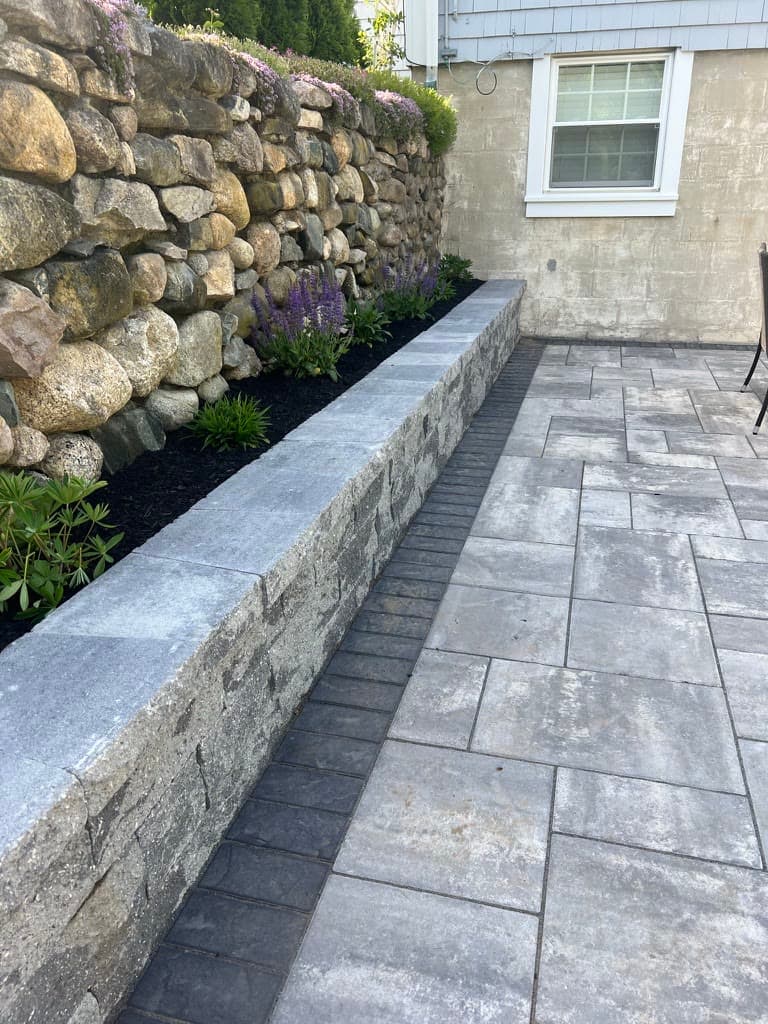 Paver patio beside a low seating wall and natural stone retaining wall