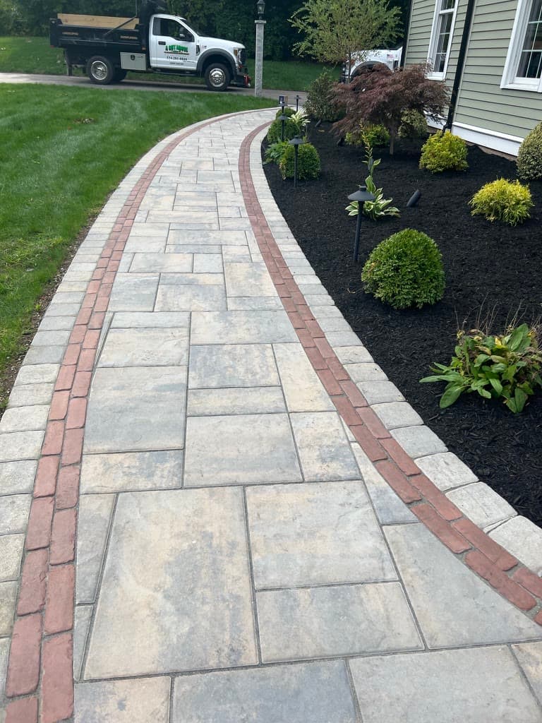 Curved paver walkway with a contrasting brick accent border and planting beds