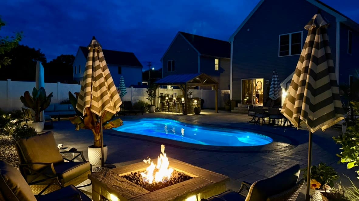 Finished poolside paver patio with a fire pit and evening lighting