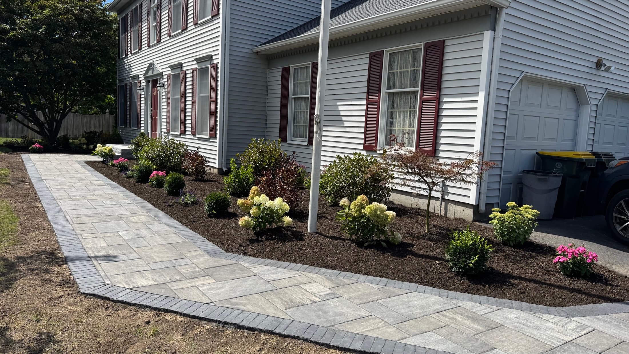 Wide finished paver walkway bordered by fresh mulch, shrubs, and flowers
