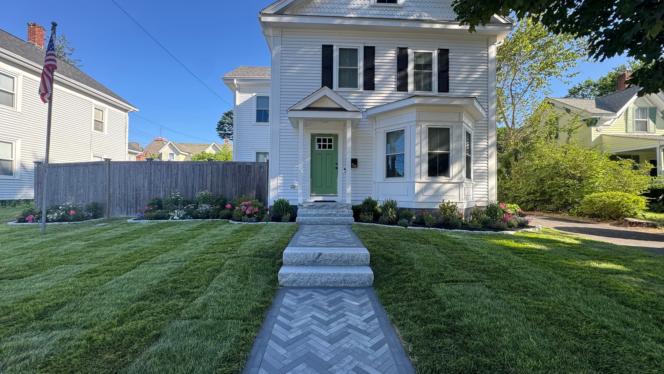 Herringbone paver front walk with granite steps, new lawn, and flowering beds