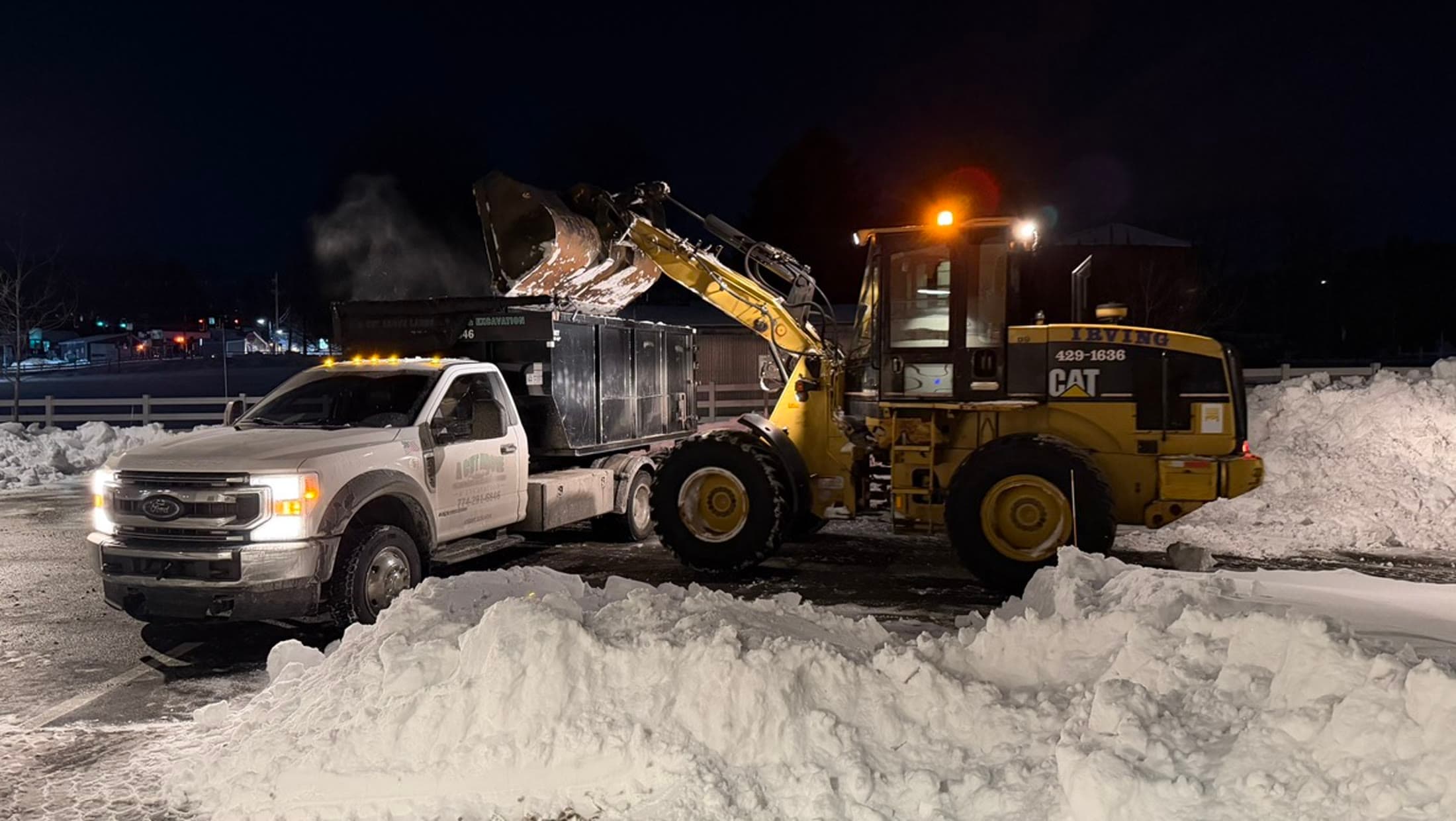 Wheel loader and plow truck removing snow from a commercial property at night