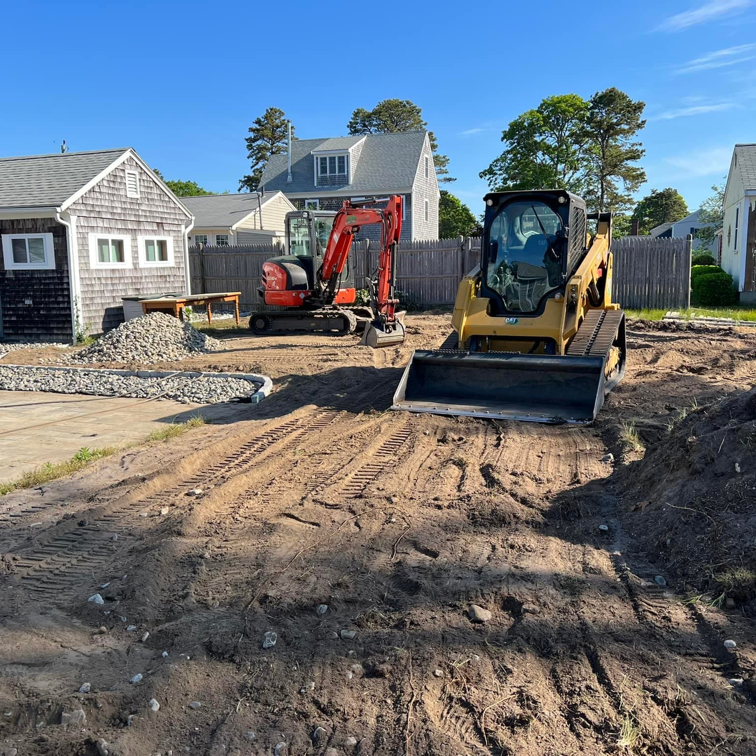 Compact excavator and track loader preparing a residential yard